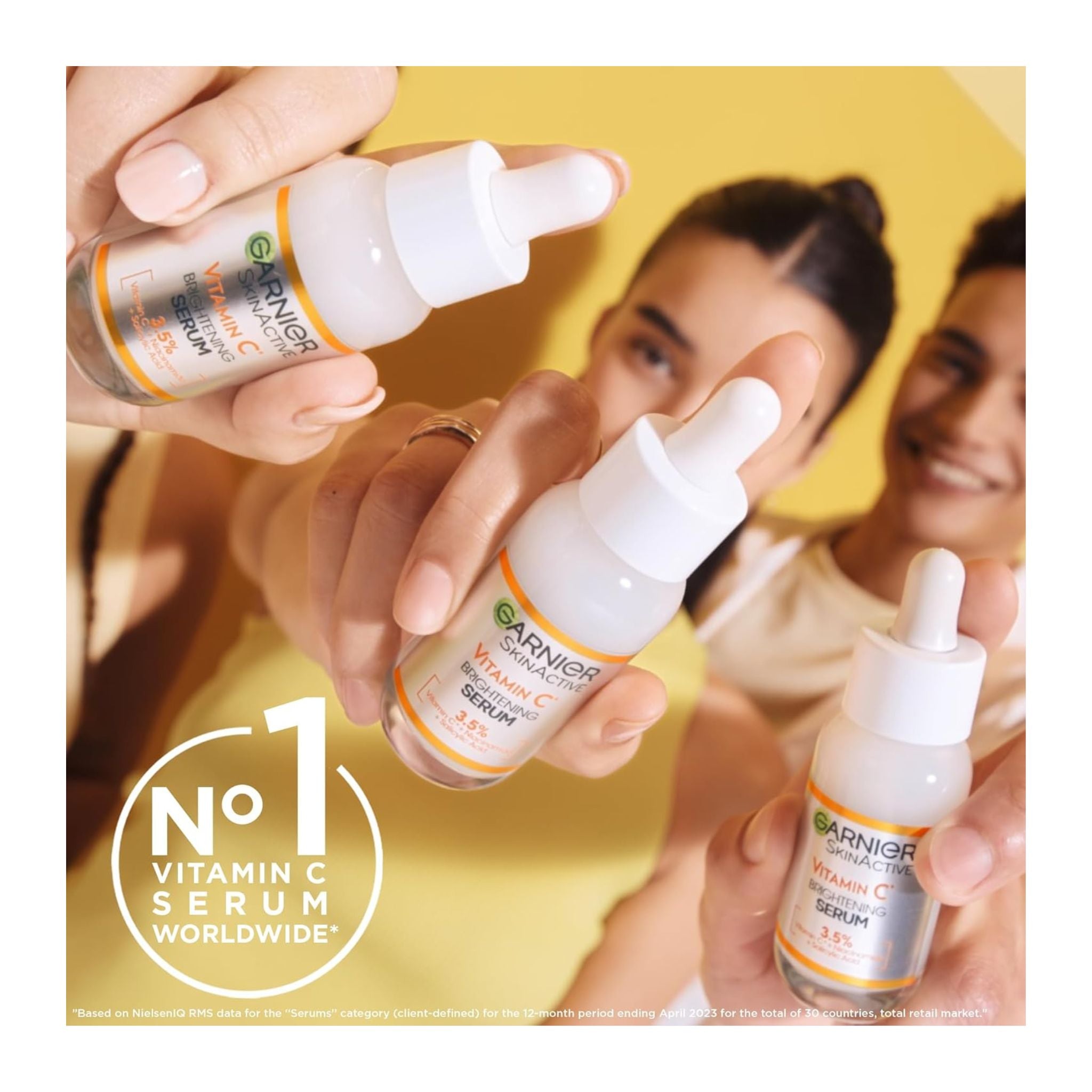 Three people holding Garnier Vitamin C serum bottles against a yellow background