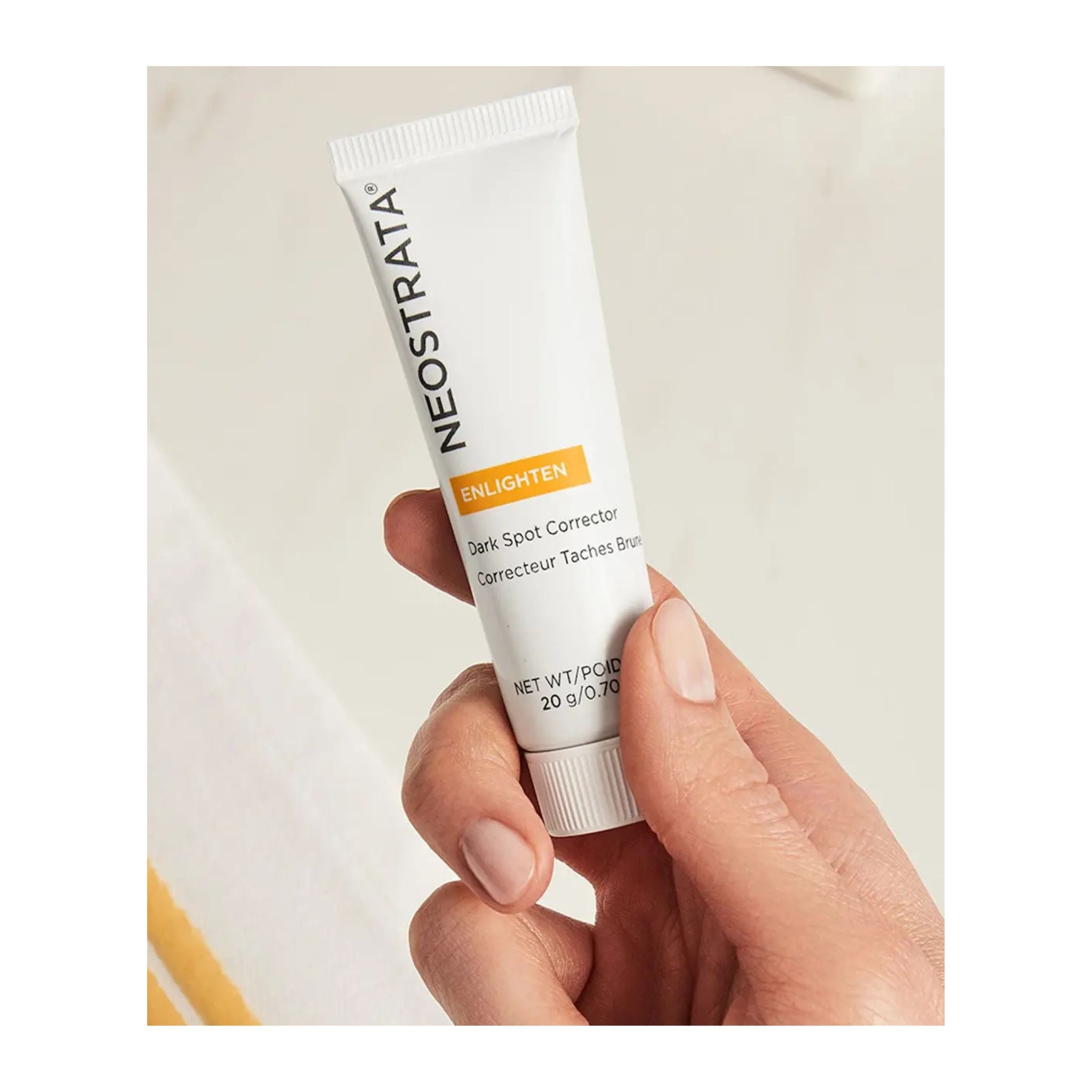Hand holding a NeoStrata Enlighten Dark Spot Corrector tube against a neutral background