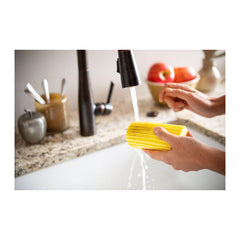 Person washing a yellow sponge under running water in a kitchen sink.