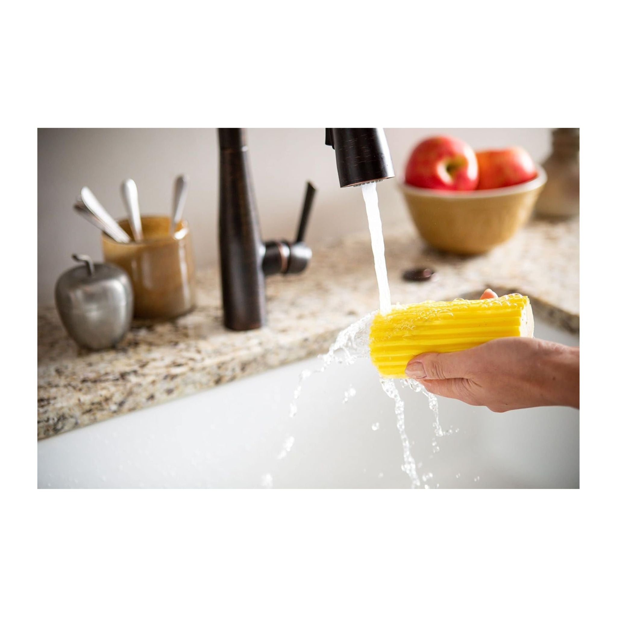 Person washing a yellow sponge under running water in a kitchen sink.