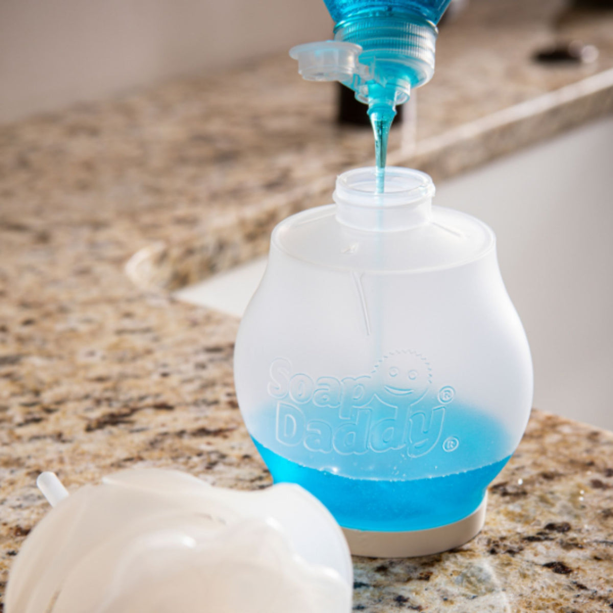 Blue liquid being poured into a clear bottle labeled 'Delux' on a marble countertop.