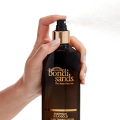Hand holding a bottle of Bondi Sands Everyday Liquid Gold tanning oil against a white background