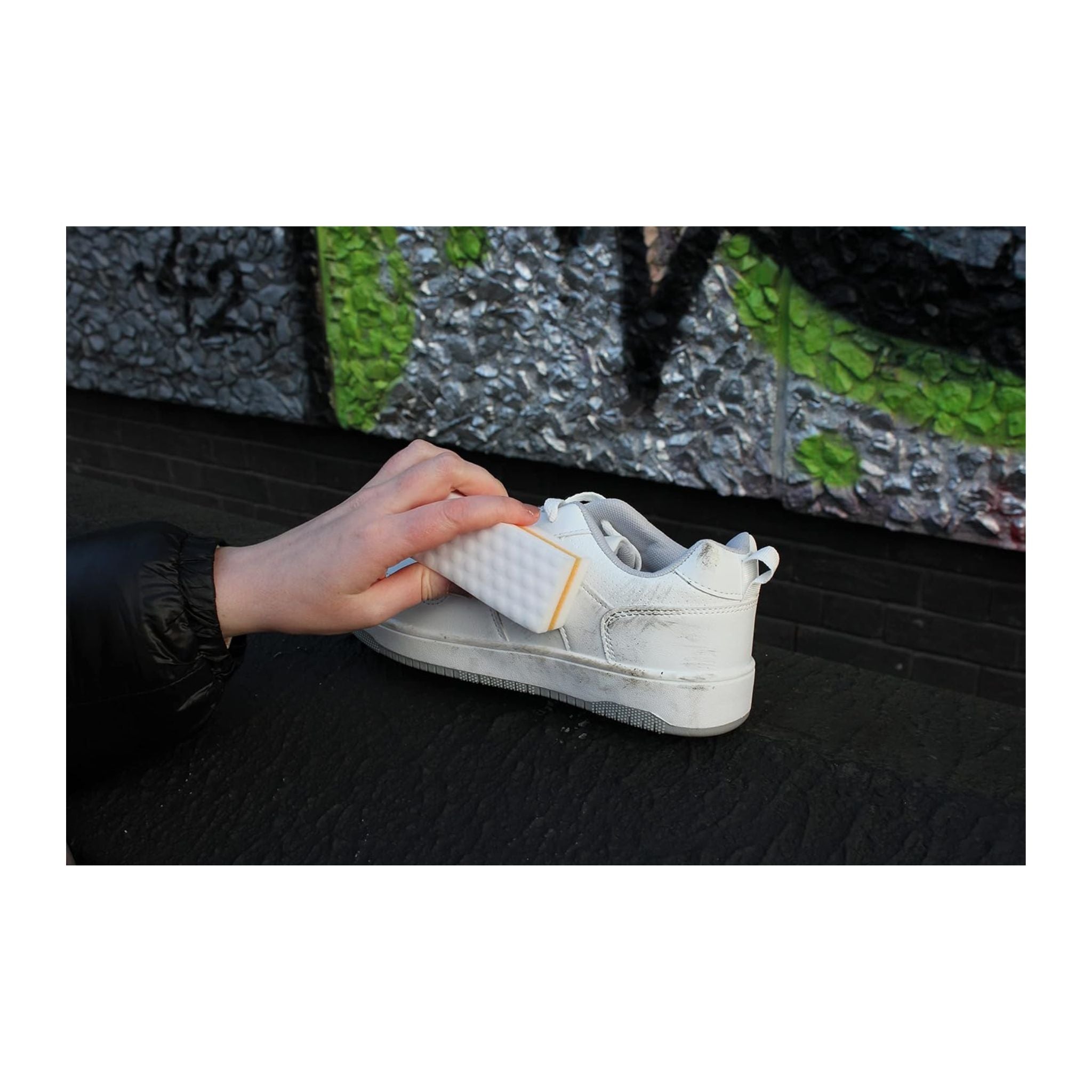 Person holding a white sneaker with a sock on a black surface